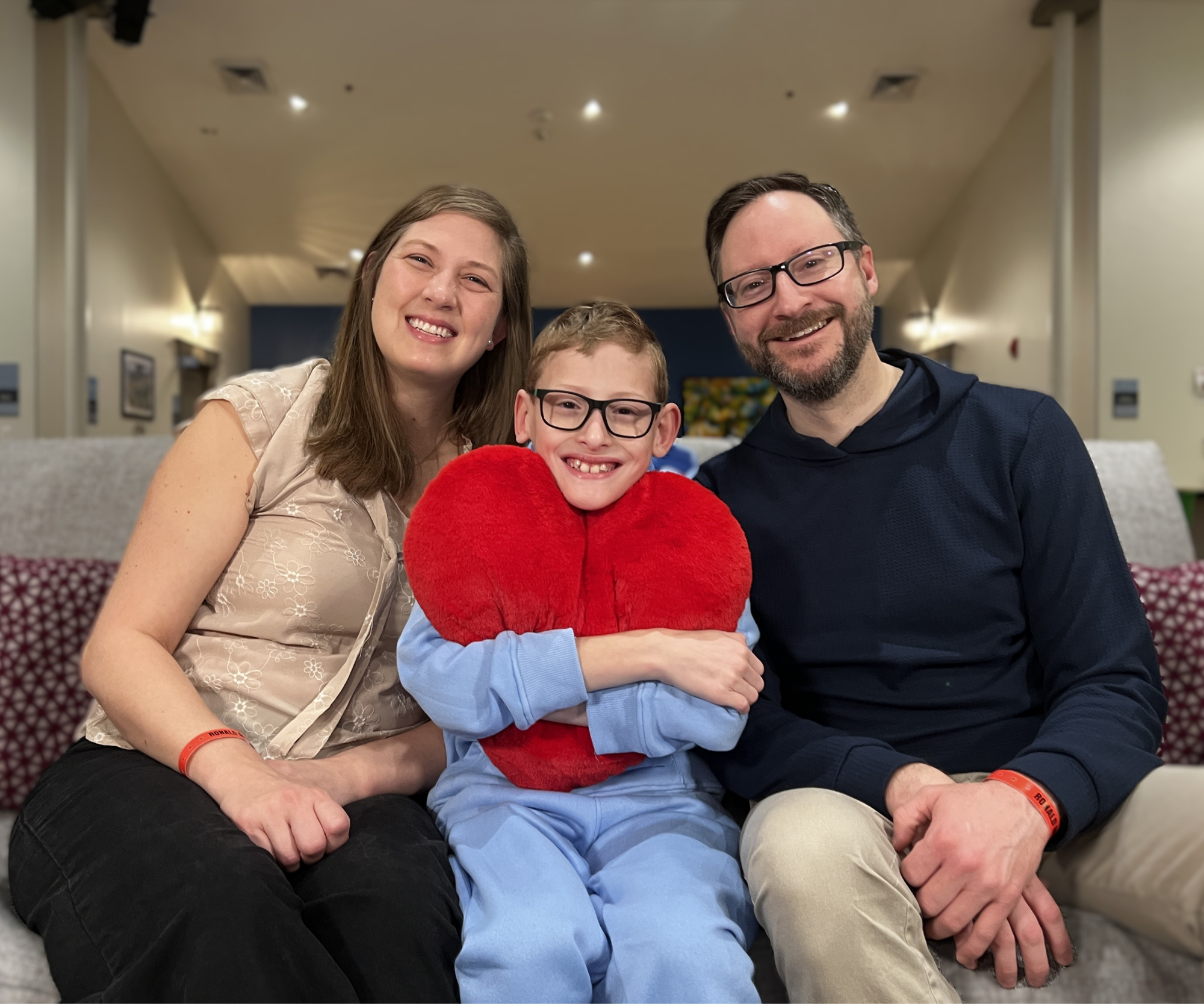 Watson family smiling and holding a heart pillow